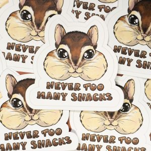 Photo of many stickers. The design is of an eastern chipmunk with it's cheeks full. It is rendered semi-realistically with large shiny eyes. Lettering underneath reads "Never Too Many Snacks".